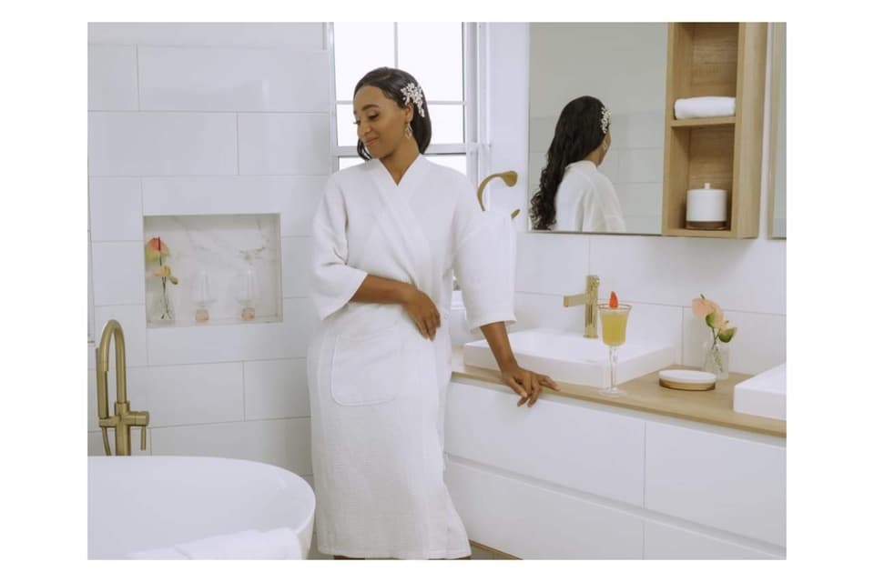 A guest in a white robe at the vanity of the primary bathroom at Bay Vista Villa