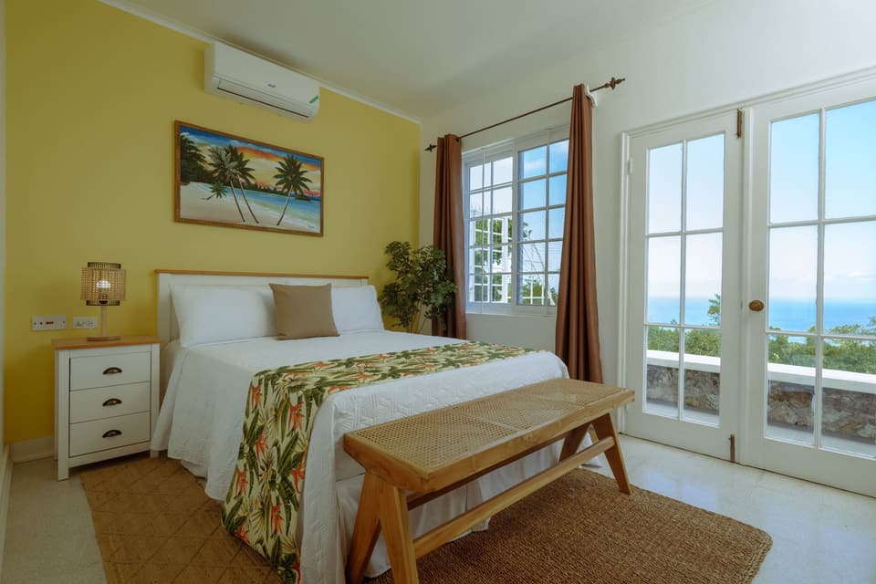 The Yellow Bird Room at Bay Vista Villa, painted warm yellow, with French doors to the sea view