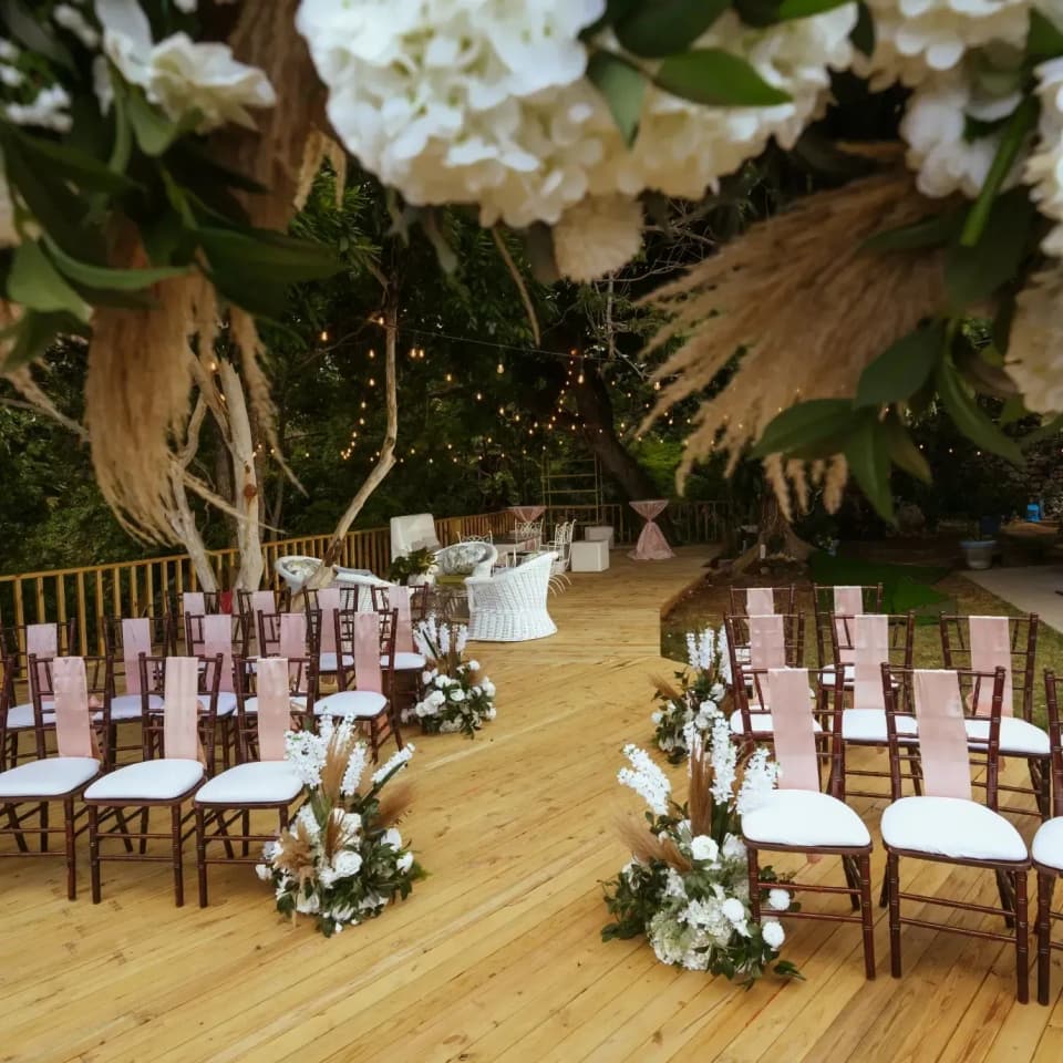 A ceremony set on the deck at Bay Vista Villa with pampas grass, white flowers and blush chair sashes