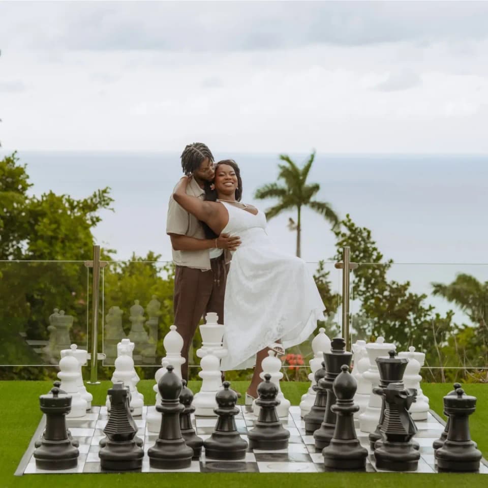 A couple embracing beside the giant chess set at Bay Vista Villa with the sea behind