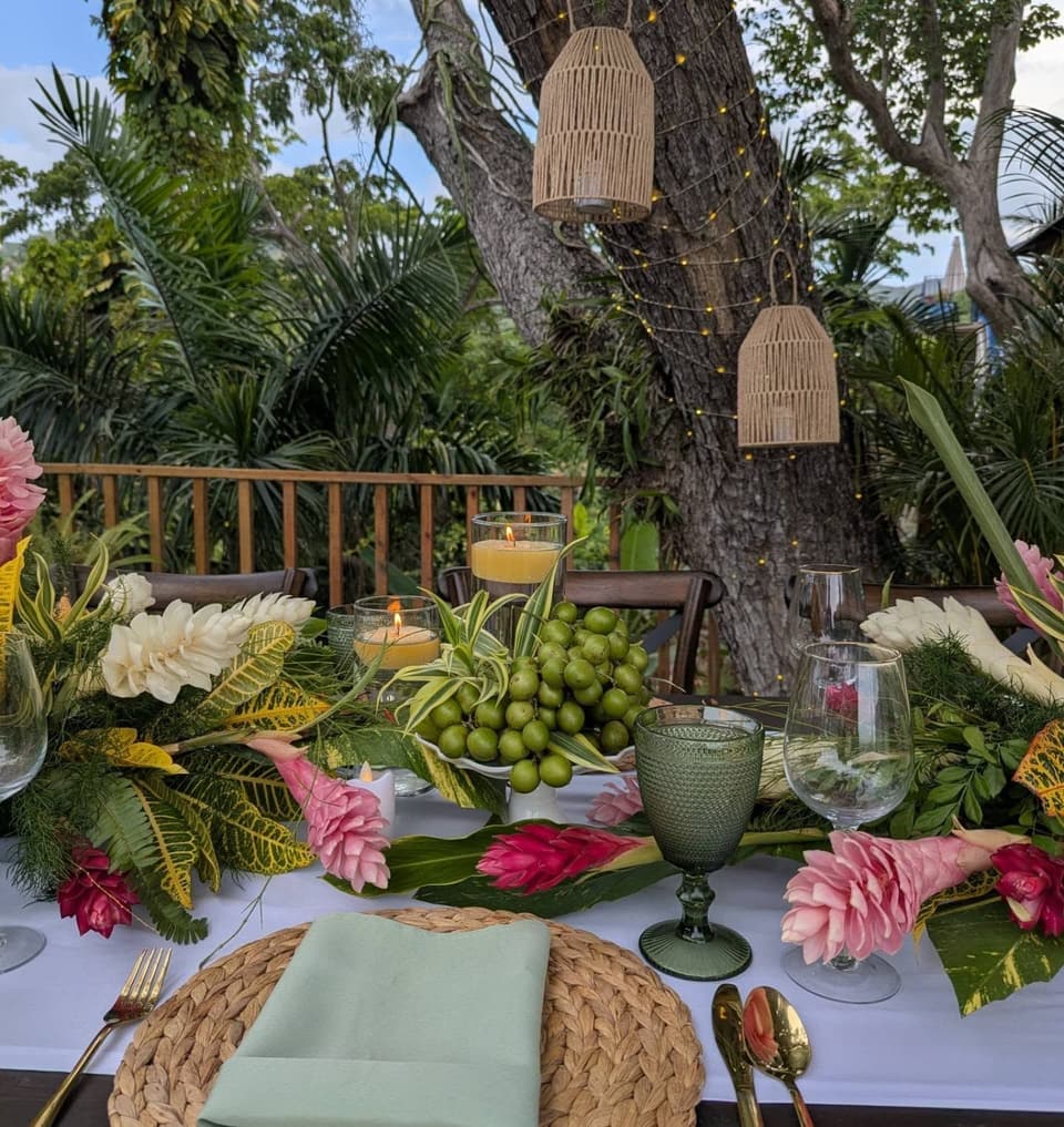 Heliconia and ginger lilies, woven placemats and green goblets on the deck table at Bay Vista Villa