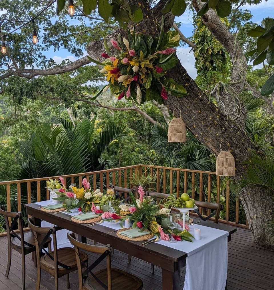 A long dinner table set with tropical flowers on the deck at Bay Vista Villa, under the great tree