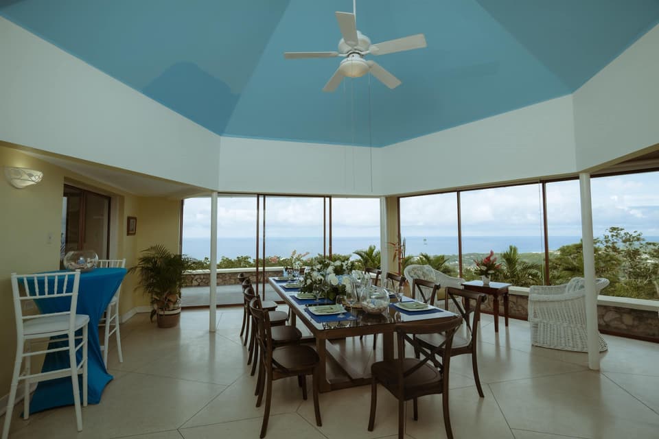 The glass-walled dining room at Bay Vista Villa with a long table set for dinner and the sea beyond