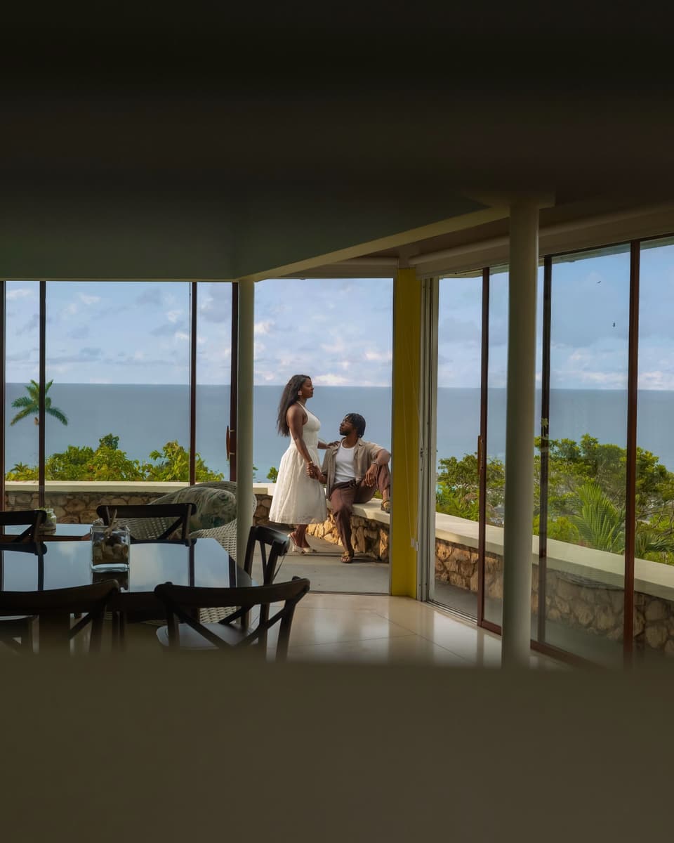 A couple silhouetted in the glass-walled dining room at Bay Vista Villa with the sea behind them