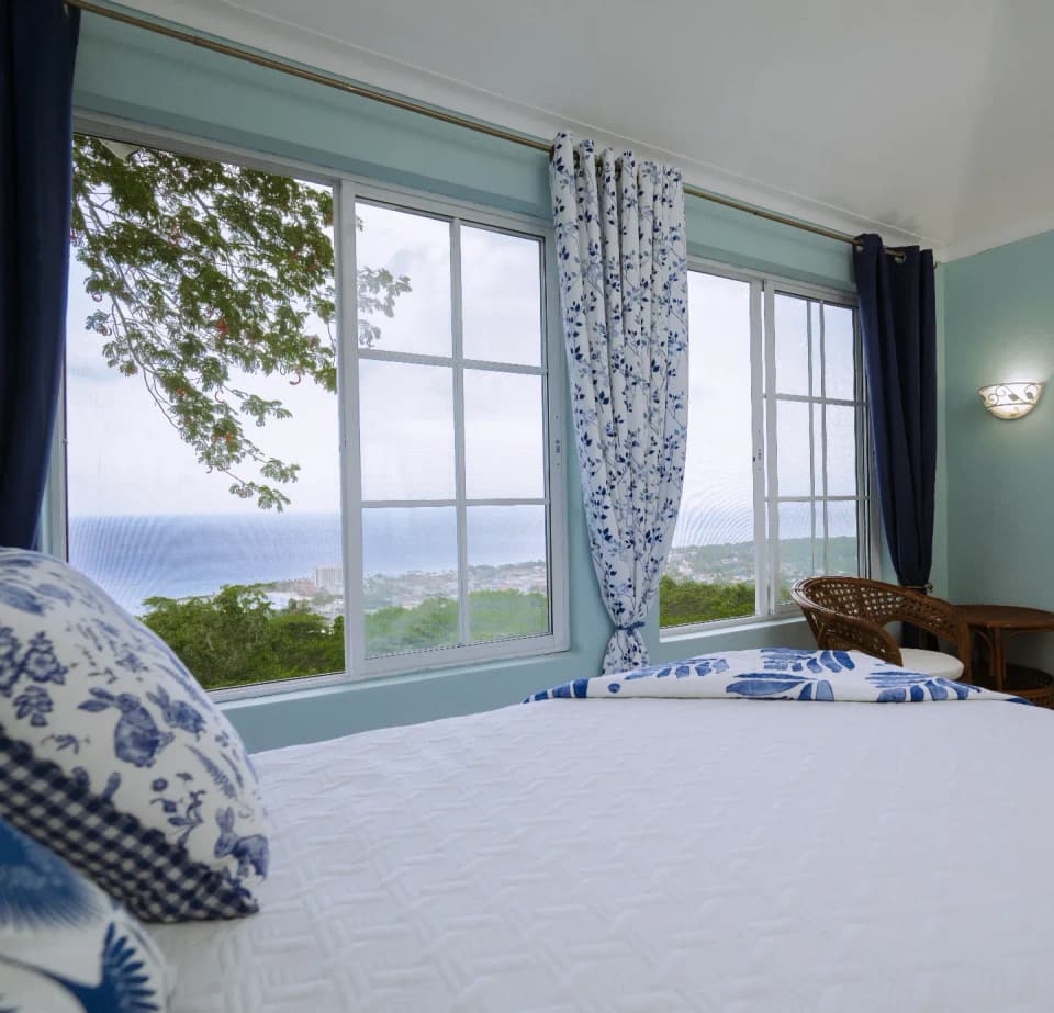 A bedroom window at Bay Vista Villa with the bay of Ocho Rios beyond the curtains